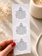 Load image into Gallery viewer, 2 inch round candle warning stickers on a strip, black and white safety labels for handmade candle jars and candle packaging.
