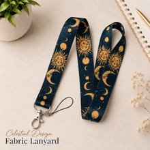 Load image into Gallery viewer, Celestial design fabric lanyard with navy blue and gold sun, moon and star pattern, silver clasp and keyring, styled on a neutral desk background.
