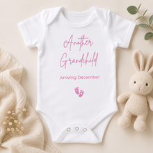 Load image into Gallery viewer, White baby onesie with pink text reading “Another Grandchild Arriving December” and pink baby footprints, styled in a soft neutral flat lay with a cream bunny toy and beige blanket.

