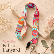 Load image into Gallery viewer, Indigenous design fabric lanyard with bright pink, turquoise, orange and yellow pattern, silver clasp and keyring, styled on a neutral flat lay background.

