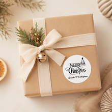 Load image into Gallery viewer, Personalised Merry Christmas sticker on kraft wrapped Christmas gift with neutral ribbon and festive greenery.
