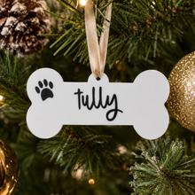 Load image into Gallery viewer, Personalised dog bone Christmas bauble with custom pet name and paw print hanging on a festive tree.

